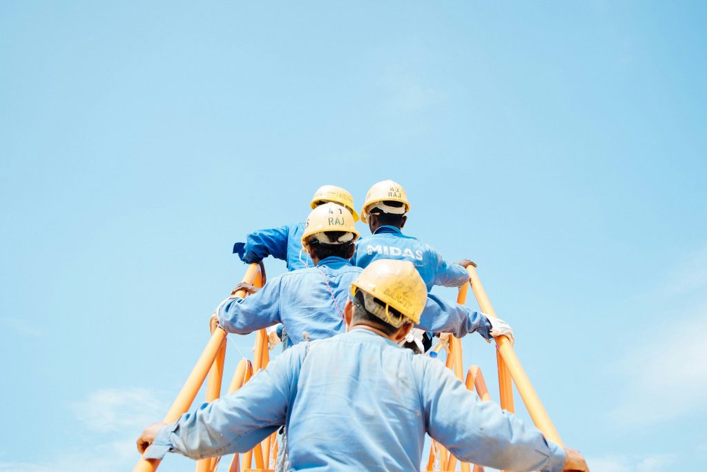Construction workers in blue uniforms and helmets climbing an orange structure.