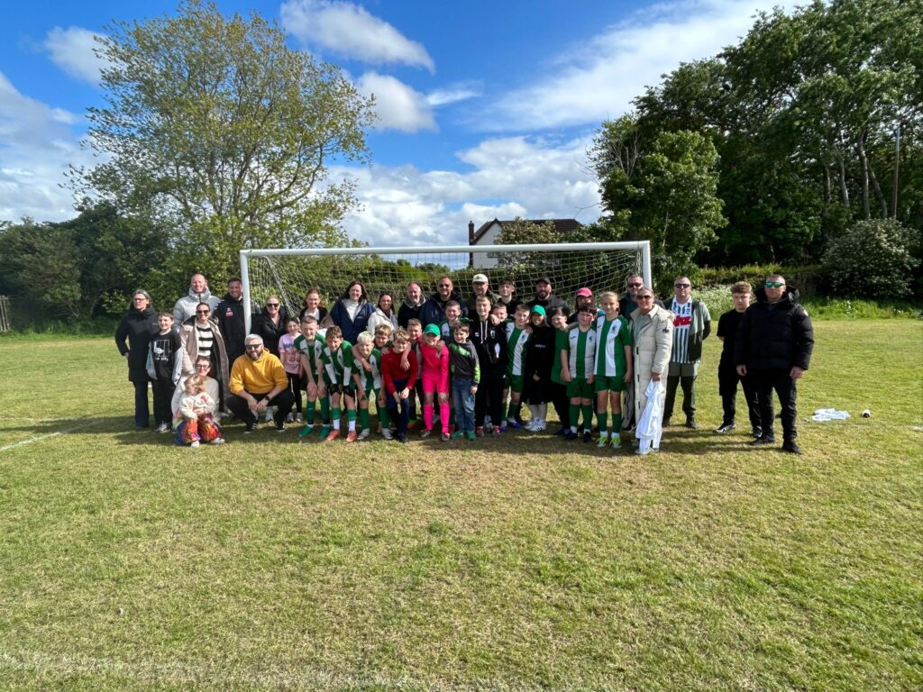 Blyth Spartans Juniors players and parents standing in front of a goal at a local tournament.